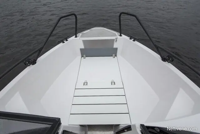 Bow of a boat showing a white non-slip deck with hatches, handrails, and calm water in the background. Nettivene.com.